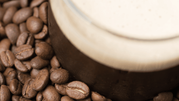 Close up of nitro coffee in a glass mug sitting on a pile of coffee beans